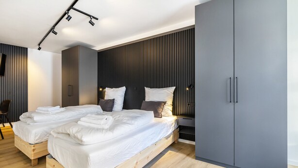 A modern bedroom with a wooden platform bed, grey wardrobe, and built-in lighting. - 3-2-1meins Röntgen Remscheid – Modern Apartment for Up to 3 Guests (Remscheid)