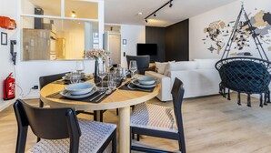 A modern living room with a dining area, a sofa, a hanging chair, and a TV mounted on the wall. - 3-2-1meins Röntgen Remscheid – Modern Apartment for Up to 3 Guests (Remscheid)