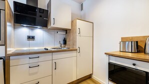 A modern kitchen with white cabinetry, a stainless steel range hood, a built-in oven, and a wooden countertop. - 3-2-1meins Röntgen Remscheid – Modern Apartment for Up to 3 Guests (Remscheid)