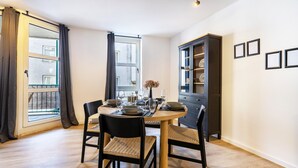 A dining area with a round table, chairs, a cabinet, and a window with curtains. - 3-2-1meins Röntgen Remscheid – Modern Apartment for Up to 3 Guests (Remscheid)