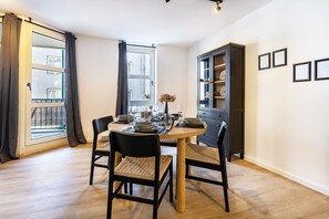 A dining area with a round table, chairs, a cabinet, and a window with curtains. - 3-2-1meins Röntgen Remscheid – Modern Apartment for Up to 3 Guests (Remscheid)