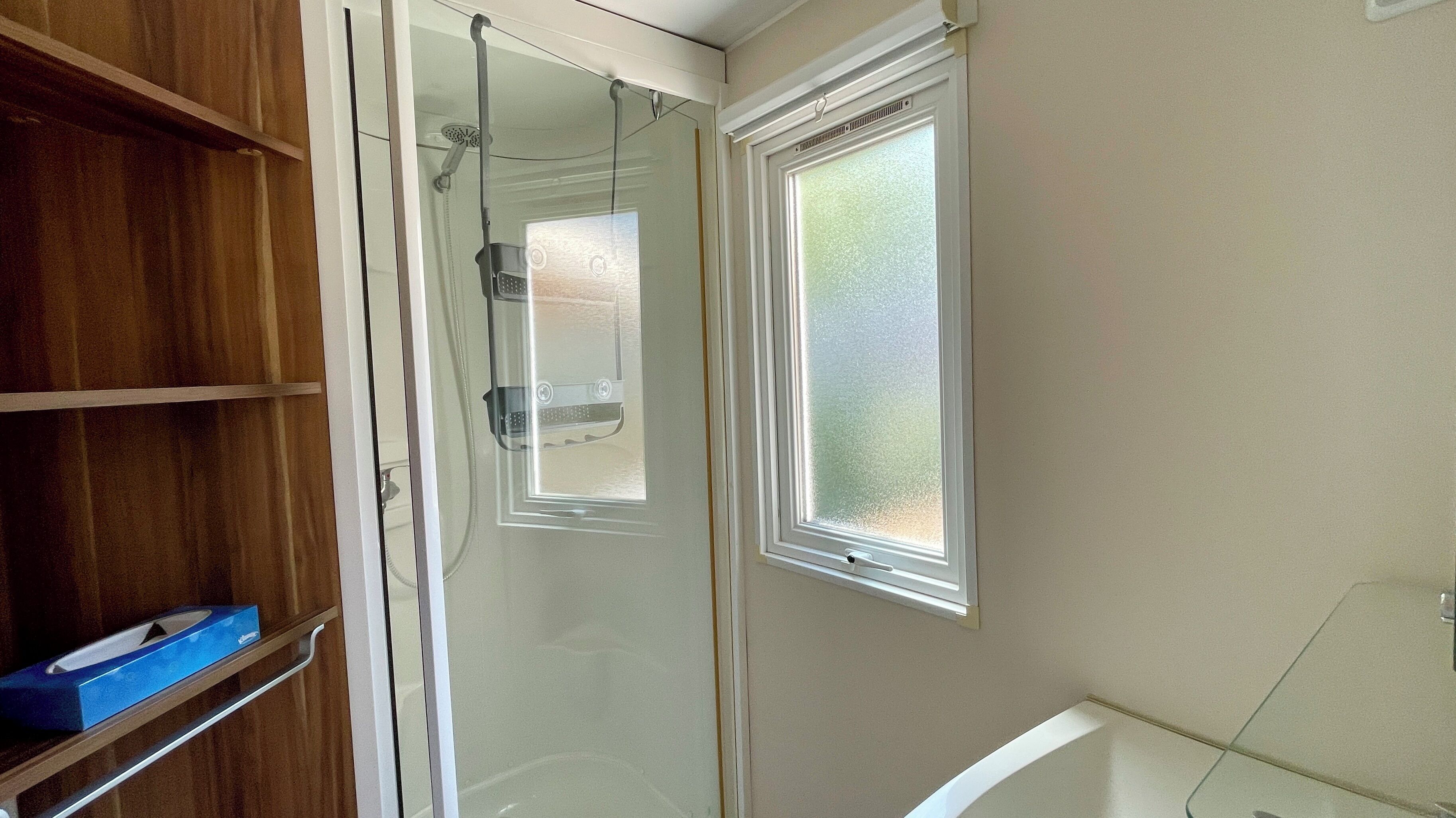 A bathroom with a shower, a window, and wooden shelving.