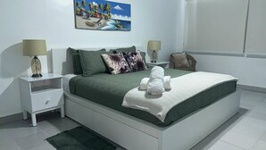 Ein ordentlich eingerichtetes Schlafzimmer mit einem Bett, zwei Nachttischen, einem Sessel und einem Bild an der Wand.