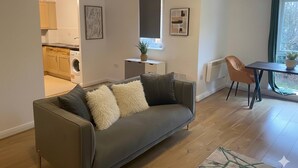 Una sala de estar moderna con un sofá gris, una mesa de comedor y una cocina visible a través de un vano abierto.