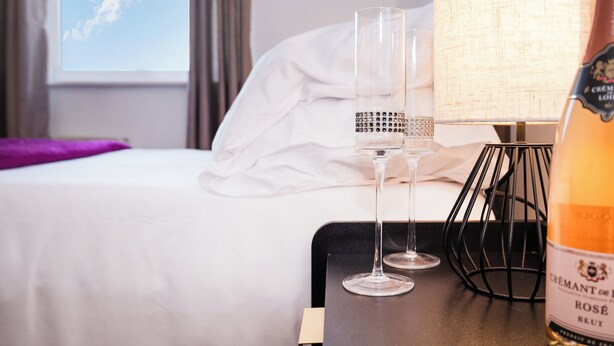 Una habitación de hotel con una cama, una mesita de noche, dos vasos, una botella de champán y una lámpara.