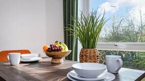 Una mesa de comedor con platos blancos, tazones y un frutero, una taza blanca y una maceta de fibra vegetal.