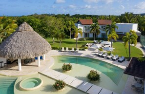 Un complexe hôtelier doté d’une piscine, de chaises longues, d’une structure à toit de chaume et d’une grande maison avec un toit rouge.