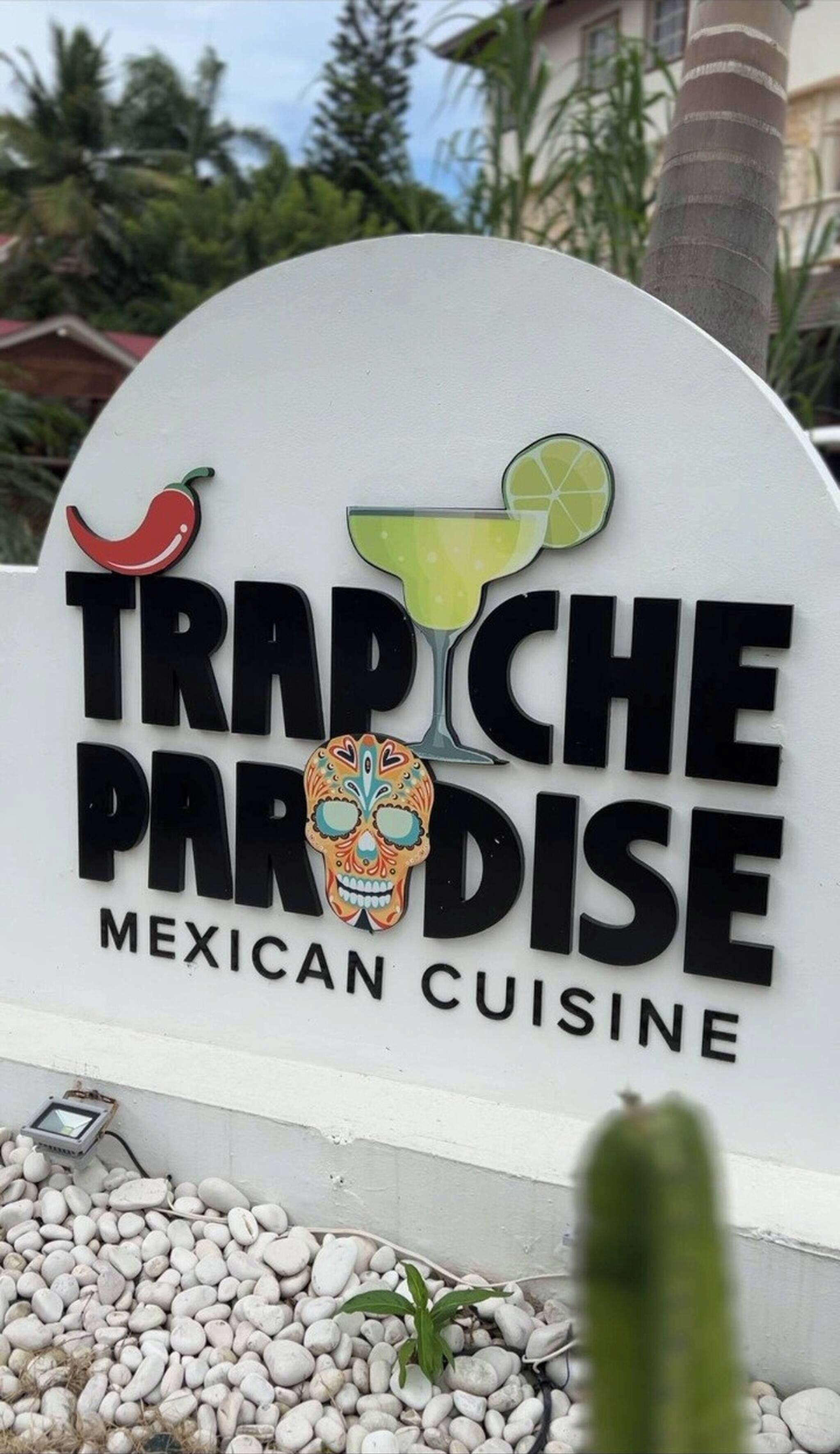 Schild für 'Trapiche Paradise Mexican Cuisine' mit einer Chili, einem Margarita-Glas und einem Zuckerschädel.