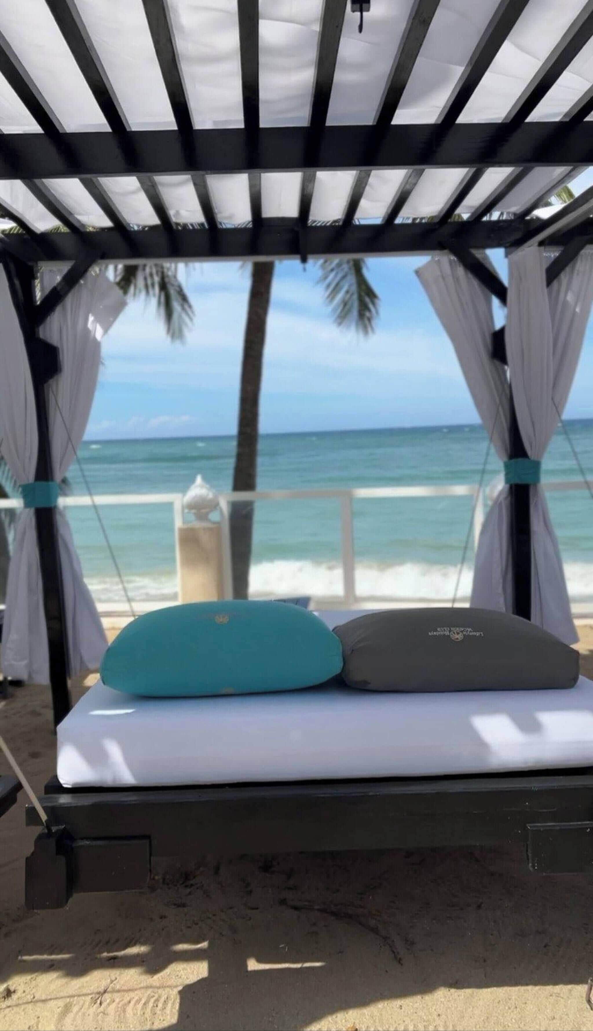 Eine Strandkabane mit Bett, weißen Vorhängen und Blick auf das Meer.
