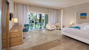 Ein Hotelzimmer mit einem großen Bett, einem Schreibtisch, einem Sessel und Blick ins Freie.