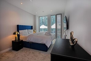 Une chambre moderne avec un lit, des tables de chevet, un bureau et une grande fenêtre donnant sur la ville.