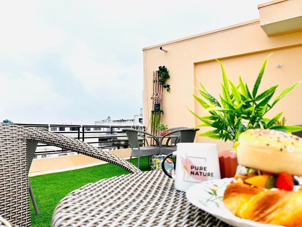 A rooftop terrace with wicker furniture, a plate of food, and a 'PURE NATURE' mug.