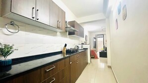 Une cuisine moderne avec des meubles en bois foncé, un plan de travail noir et un évier en acier inoxydable. On aperçoit une petite plante sur le plan de travail et un four à micro-ondes au-dessus.