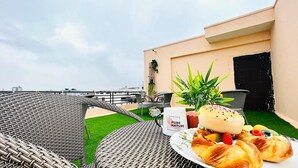 A rooftop terrace with wicker furniture, a table with pastries and a coffee mug, and a view of the city skyline. - BluO 1BHK Jaipur Terrace Garden Lift (Jaipur)
