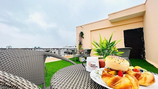 Une terrasse sur le toit, meublée de mobilier en osier, avec une table où sont disposées des pâtisseries et une tasse de café, et une vue sur le panorama urbain.