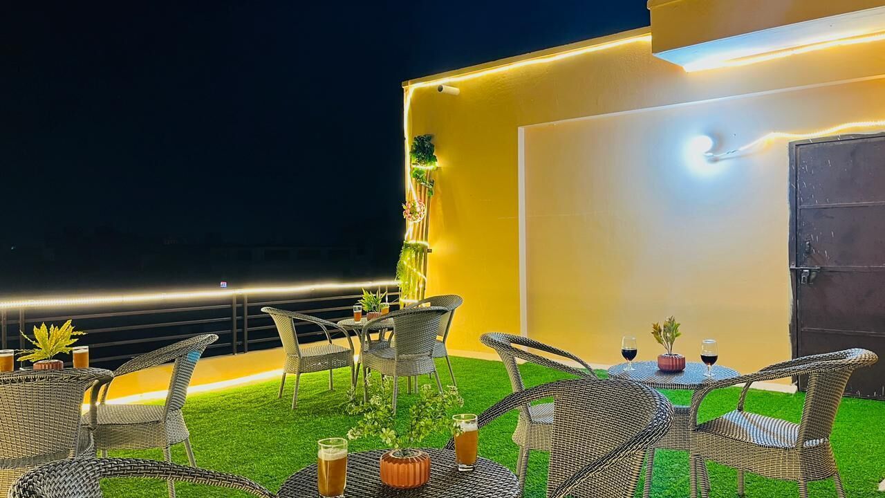 Un espacio al aire libre con sillas y mesas de mimbre, una planta pequeña en maceta y dos copas de vino sobre una mesa.