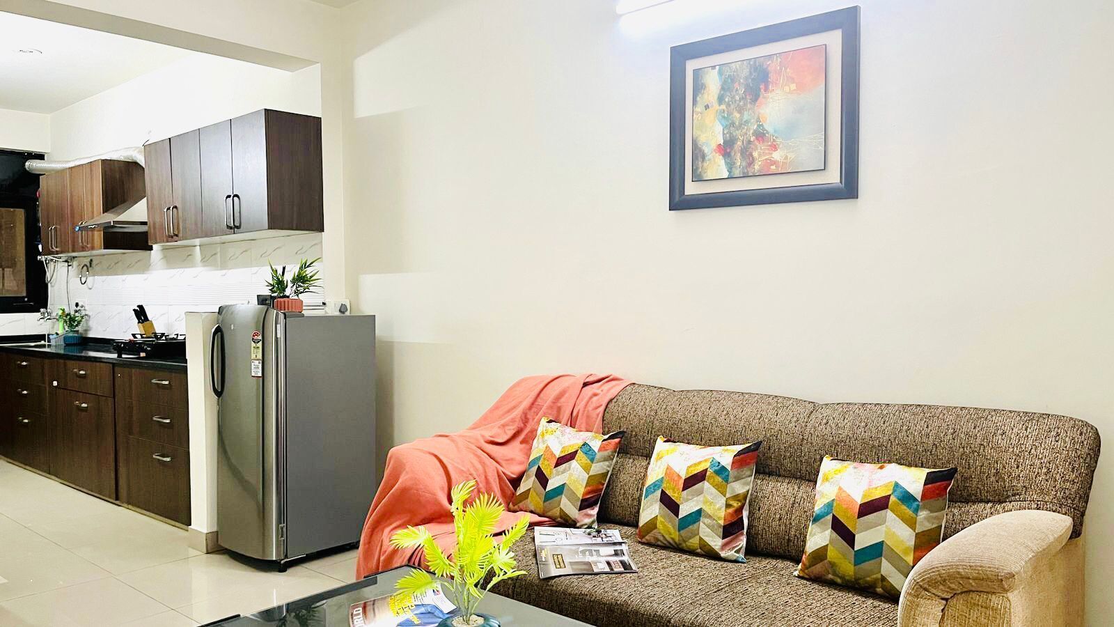 A modern living room with a sofa, cushions, a coffee table, and a kitchen area with cabinets and appliances.