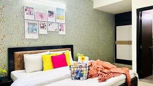 Un lit bien fait, avec une tête de lit, un mur recouvert d’un papier peint à motifs floraux et une porte sur le côté droit.