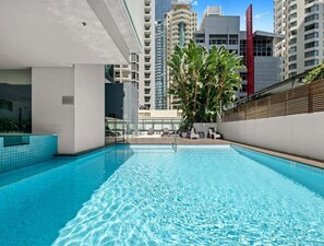 A modern indoor swimming pool with clear blue water, surrounded by a white wall and a wooden fence. - High-Floor 1BR City Escape with Balcony Views (Brisbane)