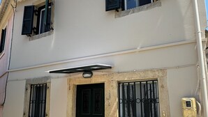 A two-story building with a beige facade, a black door, and two windows with black shutters. - Nina's House by Corfuescapes (Corfu)
