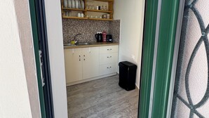 A narrow hallway leading to a kitchen with a tiled backsplash, wooden cabinets, and a black trash bin. - Nina's House by Corfuescapes (Corfu)