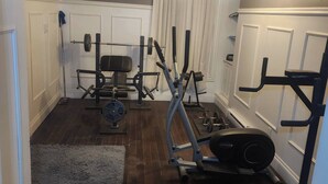 A home gym with various exercise equipment, including a bench press, dumbbells, and a stationary bike. - Room-private Master Room in a Quiet Hous (Woodstock)