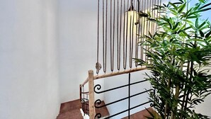 Un escalier avec une main courante en bois et des balustres en métal, menant à un palier surmonté d’une barrière verticale faite de cordes.