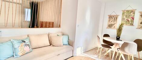 A modern living room with a sofa, a round wooden table, and a dining area with chairs.