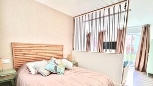 Une chambre à coucher avec une tête de lit en bois, un lit recouvert d’une couverture rose, plusieurs oreillers, une table de chevet et une fenêtre avec des rideaux.