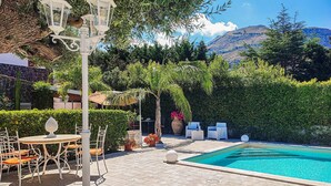 A pool area with a table and chairs, surrounded by lush greenery and a mountain view. - Stunning home in Altavilla Milicia (Altavilla Milicia)