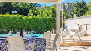A poolside area with a table set for two, chairs, and a lounge area with a view of the pool and greenery. - Stunning home in Altavilla Milicia (Altavilla Milicia)