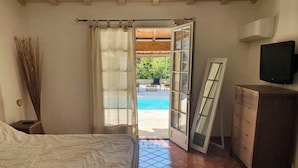 Una camera da letto con un letto, una cassettiera, un televisore e vista su una piscina all'aperto.