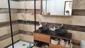 Un bagno moderno con cabina doccia in vetro, due lavabi neri, un mobile contenitore in legno e uno specchio sopra il lavabo.