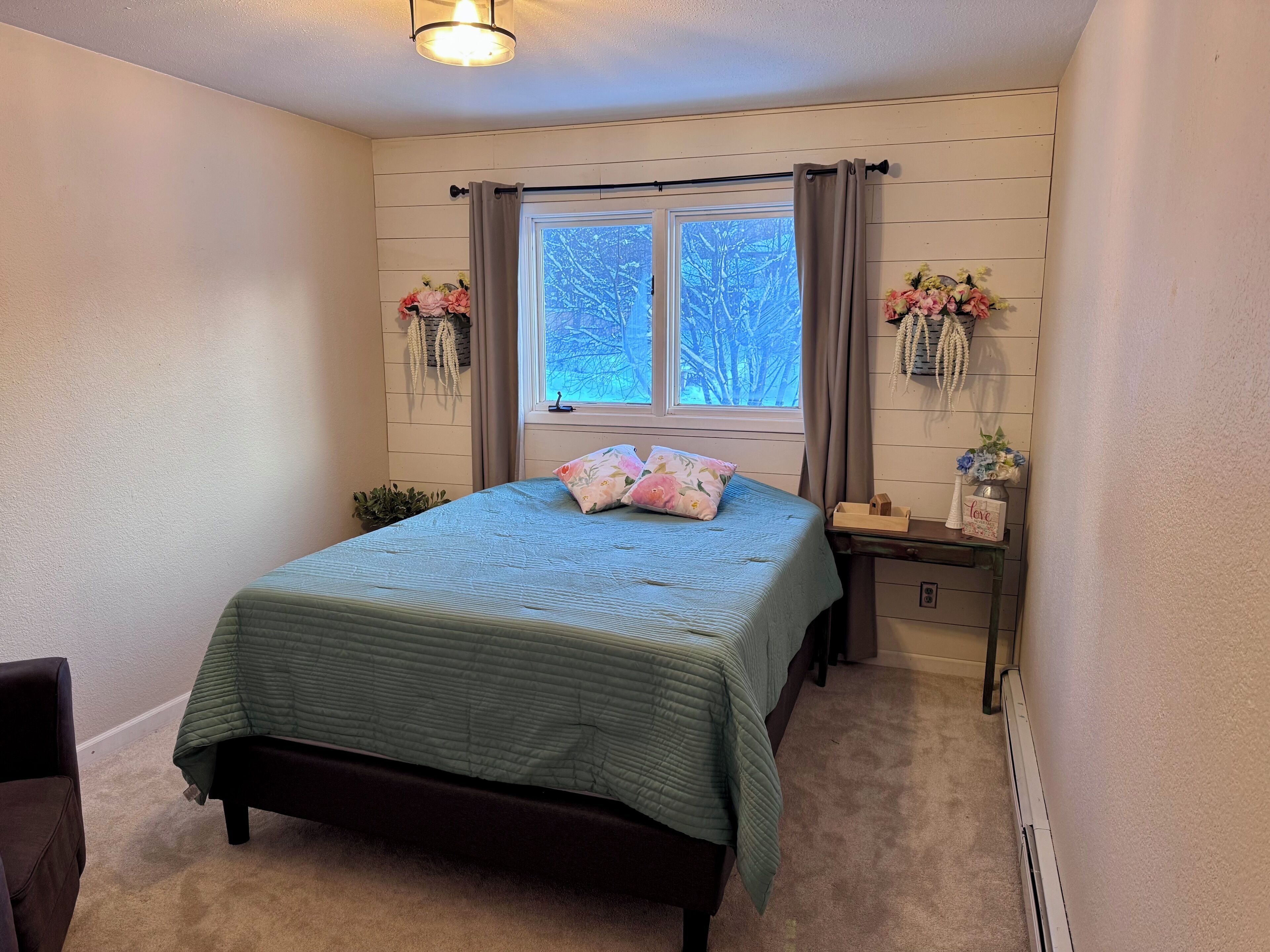 A bedroom with a bed, a nightstand, a window with curtains, and wall-mounted decorations.