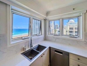A kitchen with a view of the beach and cityscape through large windows. - Surfers Paradise Ocean-View Apartment, Pool & Spa (Surfers Paradise)