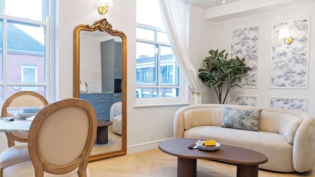Een moderne woonkamer met een bank, een salontafel, een eethoek met een tafel en stoelen, een grote spiegel en kunstwerken aan de muur.