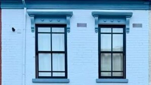 Een gebouw met twee verdiepingen, een witte gevel, een zwarte deur en een verlichte wandlamp.
