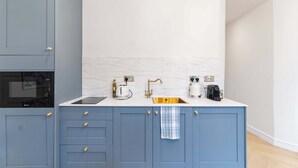 Een moderne keuken met een ingebouwde magnetron, een spoelbak met gouden kraan en een koffiezetapparaat.
