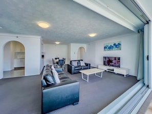 Ein modernes Wohnzimmer mit Sofa, Couchtisch, Fernseher und einem Essbereich mit Stühlen und Tisch.