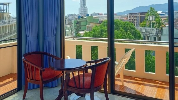 A balcony with a view of a cityscape, a table, and two chairs. - Riviera Guesthouse Patong (Patong)