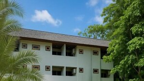 A pool area with a clear blue pool, surrounded by a beige wall and palm trees. - Riviera Guesthouse Patong (Patong)