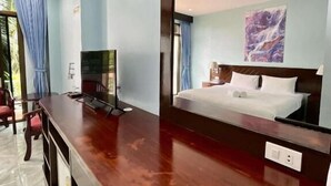 A hotel room with a wooden desk, a bed with white linens, a large mirror, and a painting on the wall. - Riviera Guesthouse Patong (Patong)