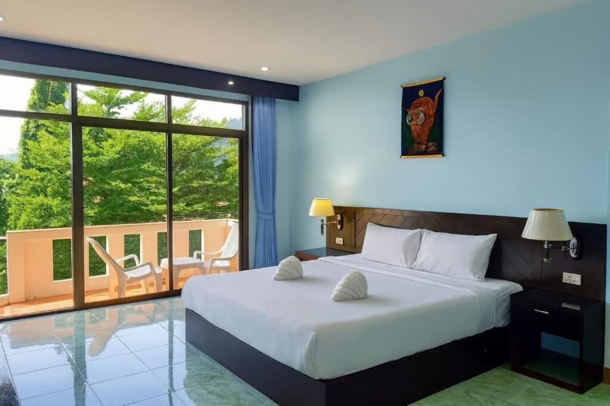 Une chambre d’hôtel avec un grand lit, deux lampes de chevet, une table de nuit et une vue sur la verdure grâce à de grandes fenêtres.