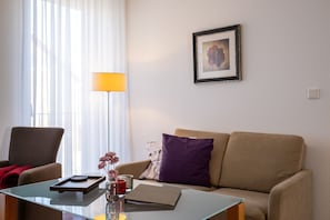 A modern living room with a glass coffee table, a beige sofa, a red chair, a floor lamp, and a framed picture on the wall.
