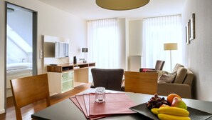 A hotel room with a dining table, chairs, a sofa, a TV, and a fruit basket. - 5-Star Comfort Holiday Home Jümmers – 'Pidder', Prime Location by the Wadden Sea National Park (Wangerland-Horumersiel)