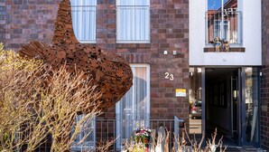 A building with a large metal sculpture in front, a brick facade, and a door marked with the number 23. - 5-Star Comfort Holiday Home Jümmers – 'Pidder', Prime Location by the Wadden Sea National Park (Wangerland-Horumersiel)