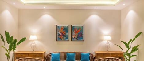 A room with a sofa set, two lamps, a ceiling fan, and two wall-mounted paintings.