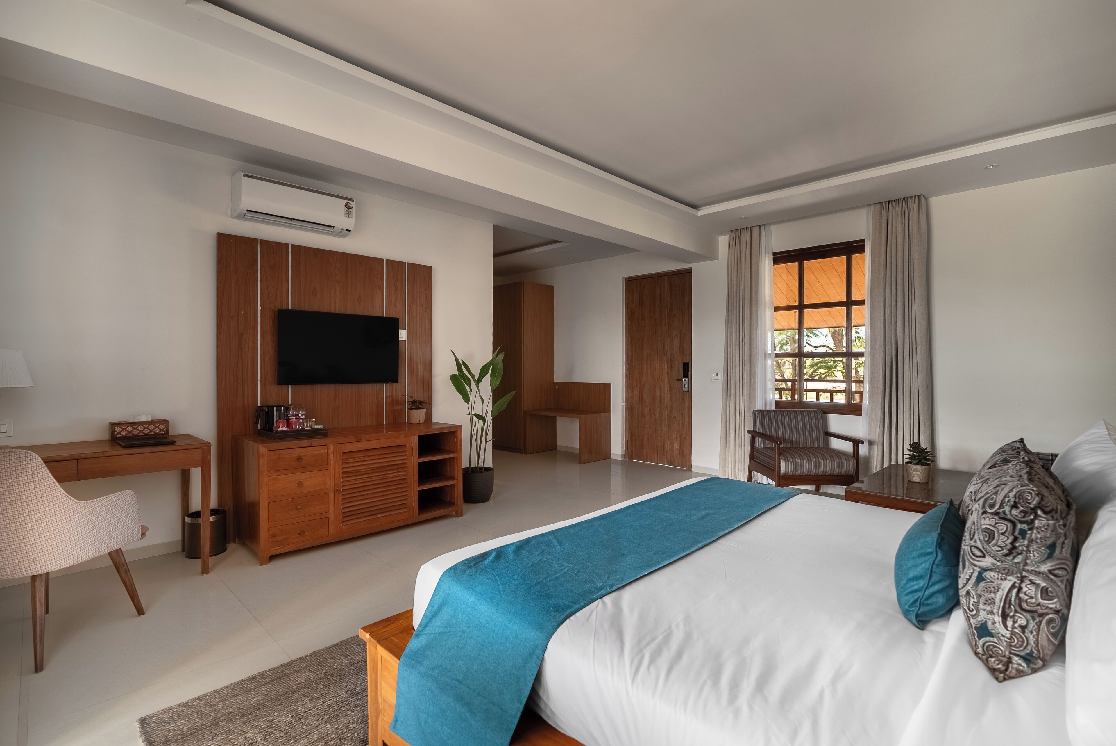 A modern hotel room with a large bed, a desk, a television, and a seating area with a view of the outdoors.