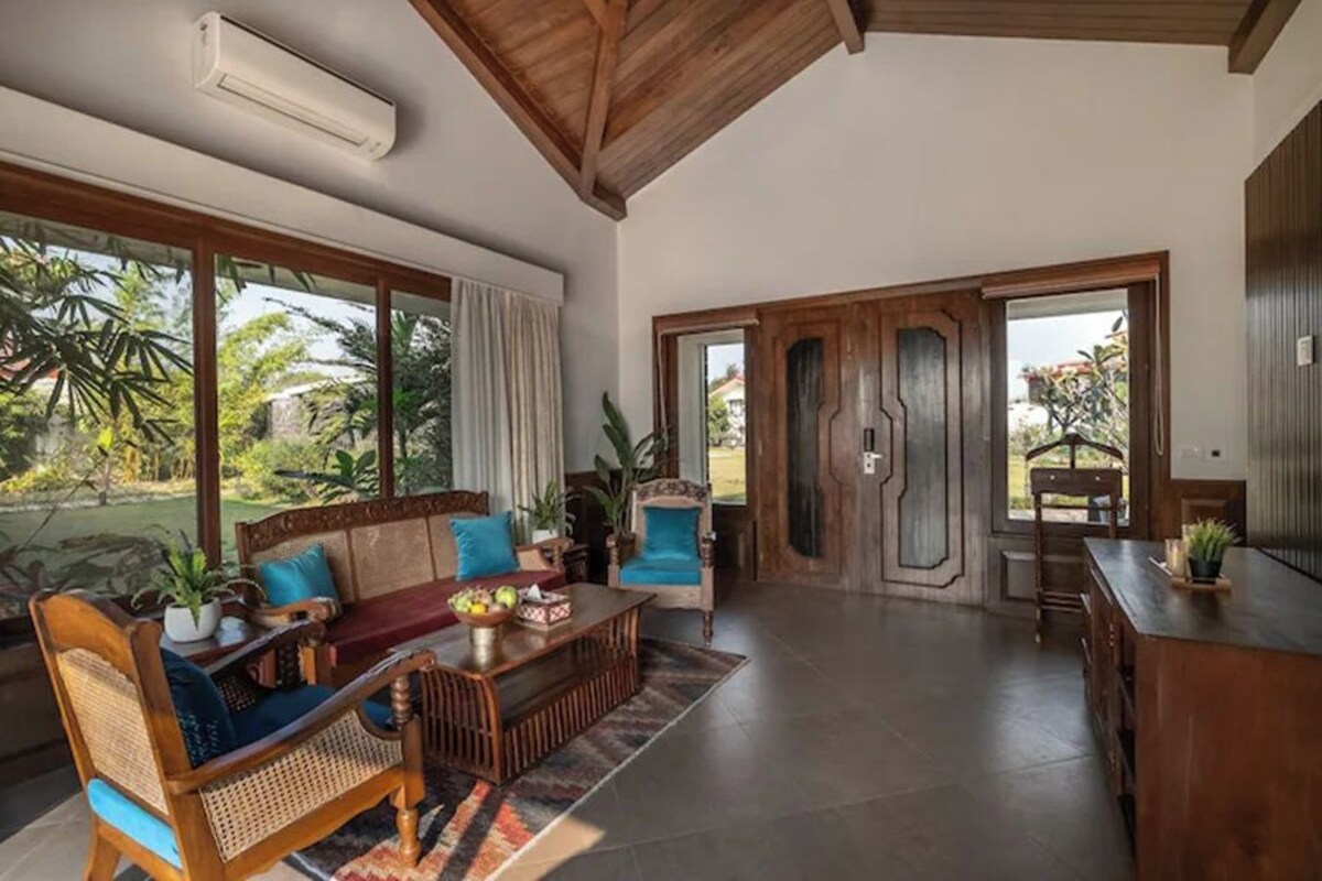 A spacious living area with a sofa, coffee table, and chairs, large windows with curtains, and a wooden door.