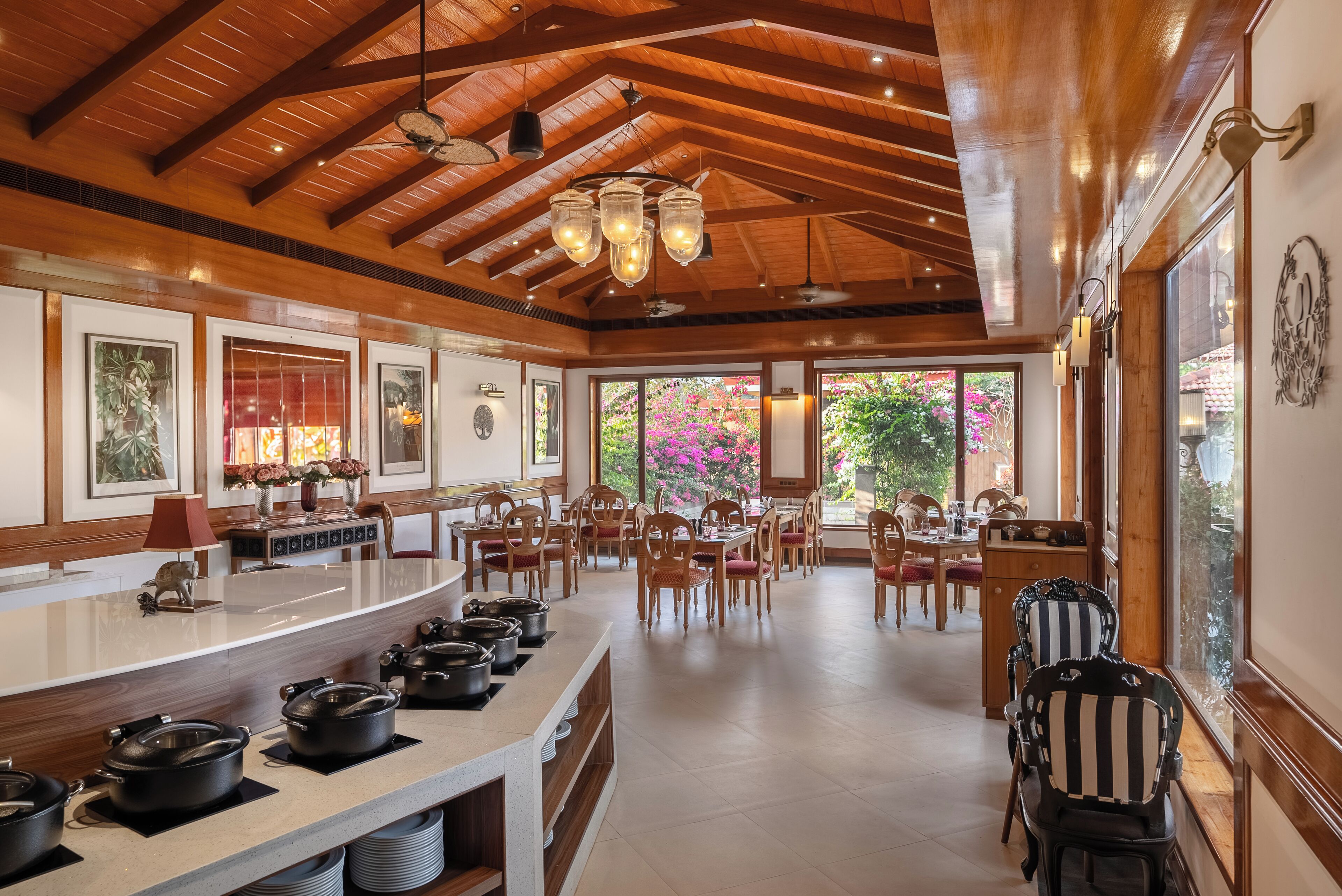A spacious dining area with wooden ceiling beams, a long counter with multiple pots, and several dining tables with chairs.